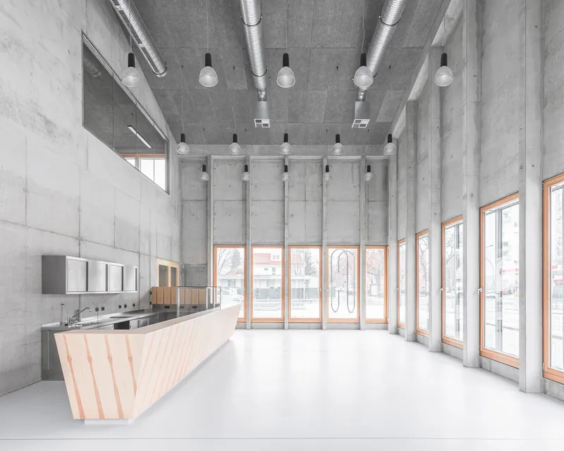 Interior lobby with faceted timber reception desk, exposed concrete walls, ceiling ducts and pendant lights