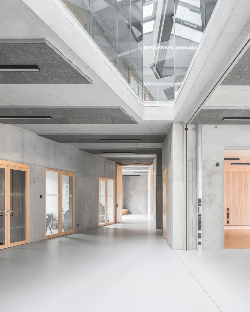 Interior corridor with central skylight, concrete beam ceiling, polished floor and timber framed doorways