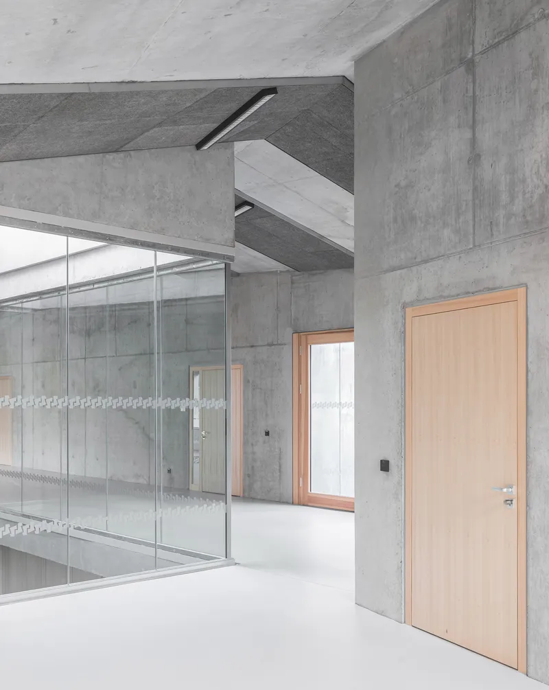 Interior detail of concrete beam junction, translucent glass partition and timber door under linear ceiling fixture