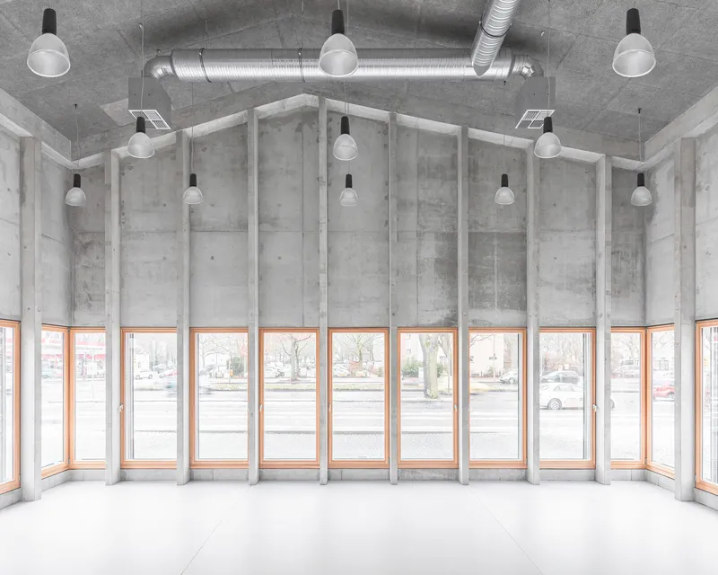 Curved interior corner with rhythmic concrete fins between timber-framed windows under exposed ductwork and pendant lights