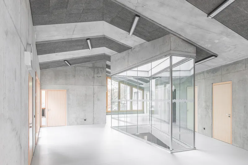 Interior hall with glass-walled enclosure beside concrete walls and stepped ceiling beams overhead