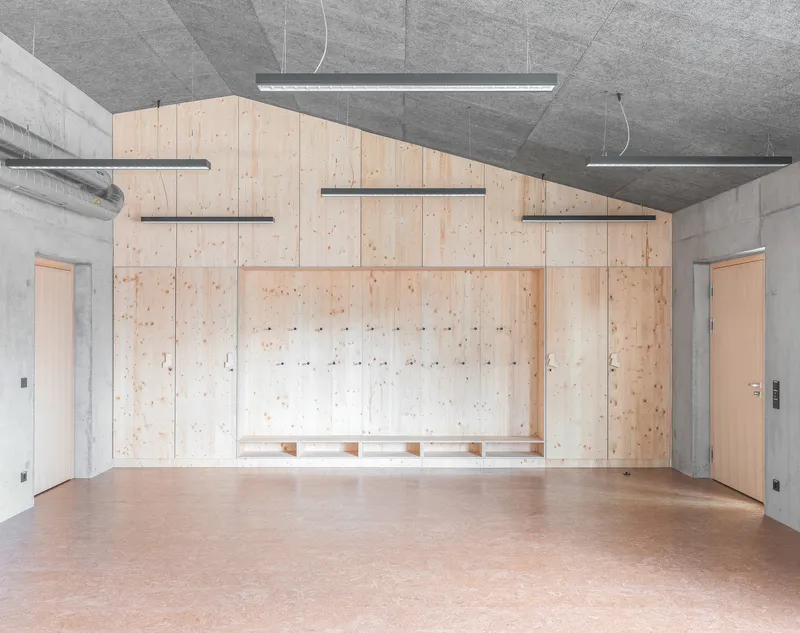 Plywood storage wall with integrated coat hooks and shelving under suspended linear lighting fixtures