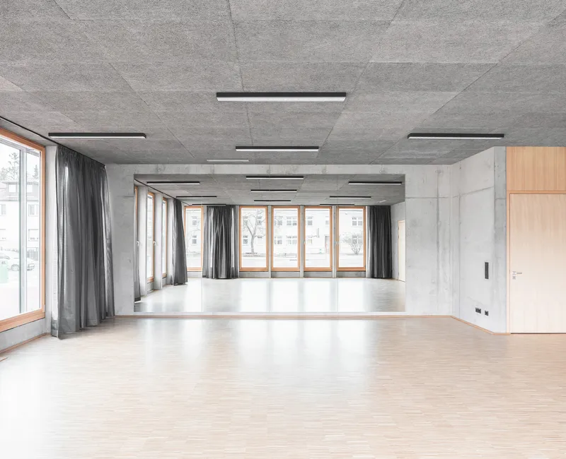 Open multipurpose room with grey curtains along timber windows and a polished concrete ceiling