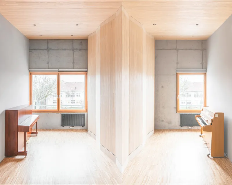 Symmetrical view of two mirrored rooms with vertical timber cladding and pianos beneath wood ceilings
