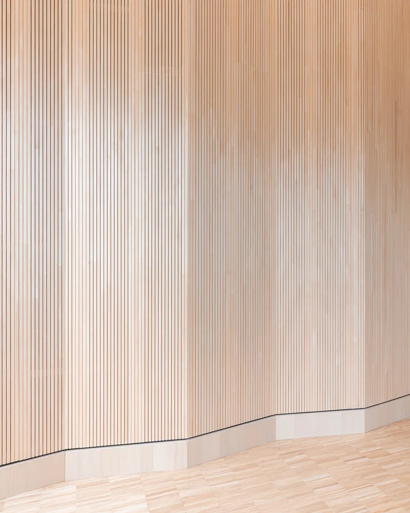 Detail of vertical timber slat wall with curved corner meeting pale wood flooring