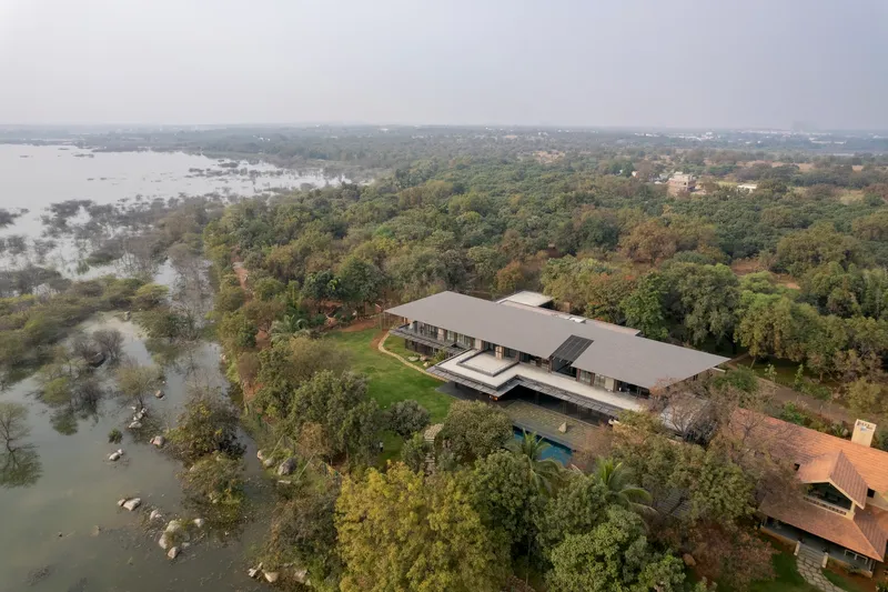 Aerial view of the grey-roofed residence nestled among dense forest and adjacent wetlands under hazy skies