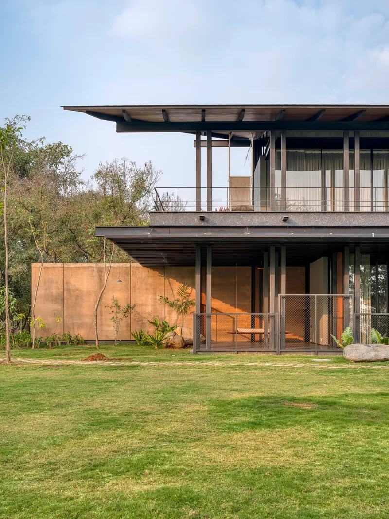 Two-story steel-framed facade with deep overhangs and rammed earth wall beside a manicured lawn