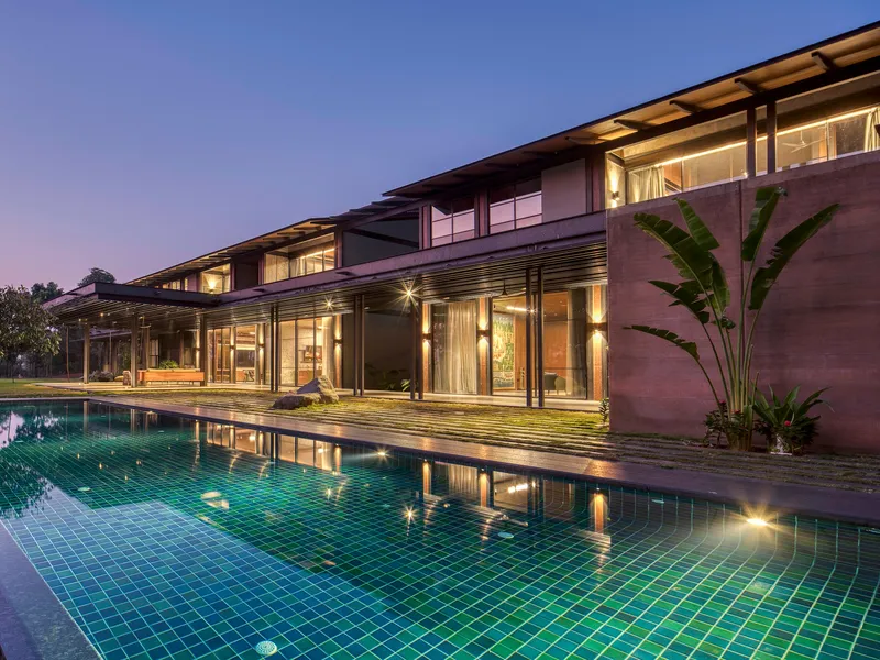 Pool deck with green tile lining reflecting the illuminated interior spaces and timber roof structure at dusk