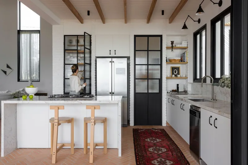 Kitchen with exposed timber ceiling beams and black steel-framed glass doors with reeded panels