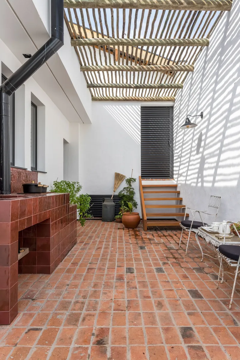 Outdoor courtyard with terracotta paving and timber pergola casting striped shadows on white walls