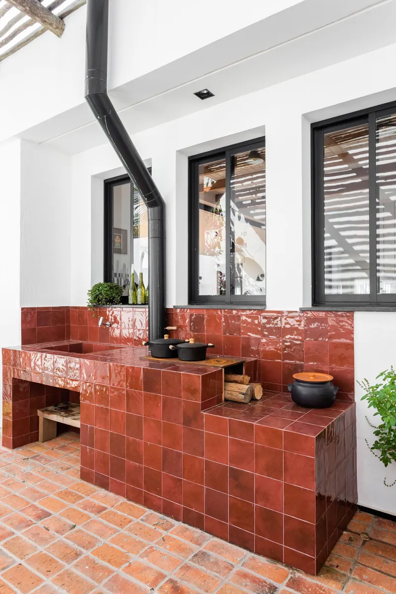 Red glazed tile kitchen counter and backsplash beneath white arched openings with black framed windows