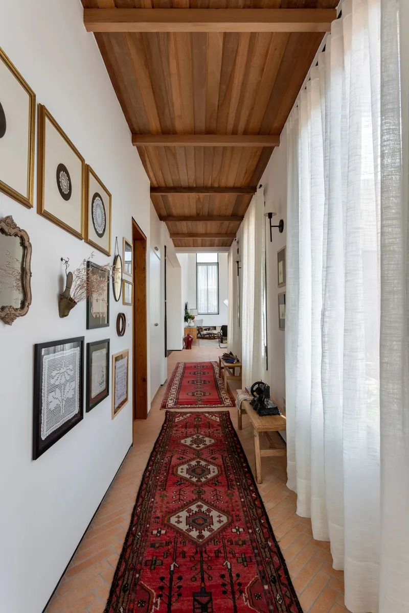 Long corridor with timber beam ceiling and sheer curtains filtering daylight along terracotta floor