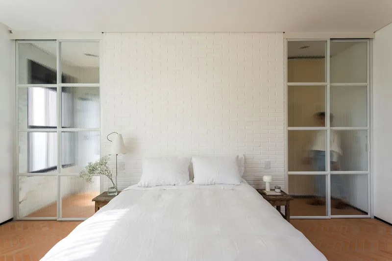 Bedroom with white tile accent wall flanked by ribbed glass sliding doors and terracotta floor