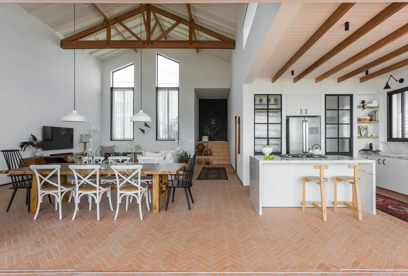 Open-plan living space with herringbone terracotta tile floor and exposed timber trusses overhead