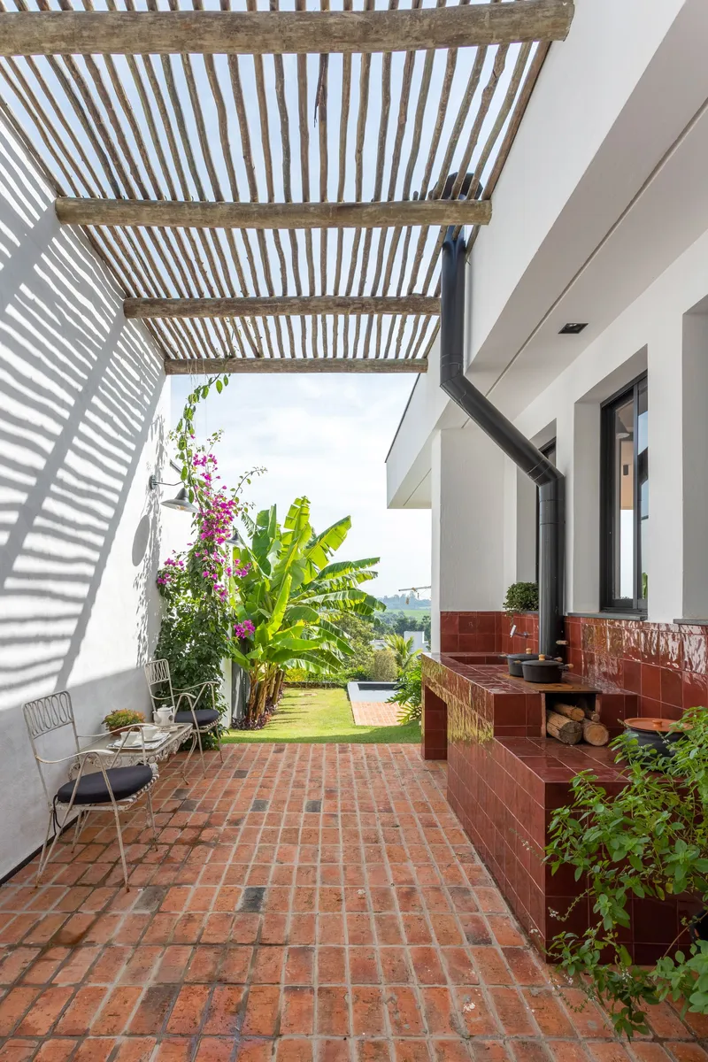 Covered terrace with timber slatted pergola casting striped shadows over terracotta pavers