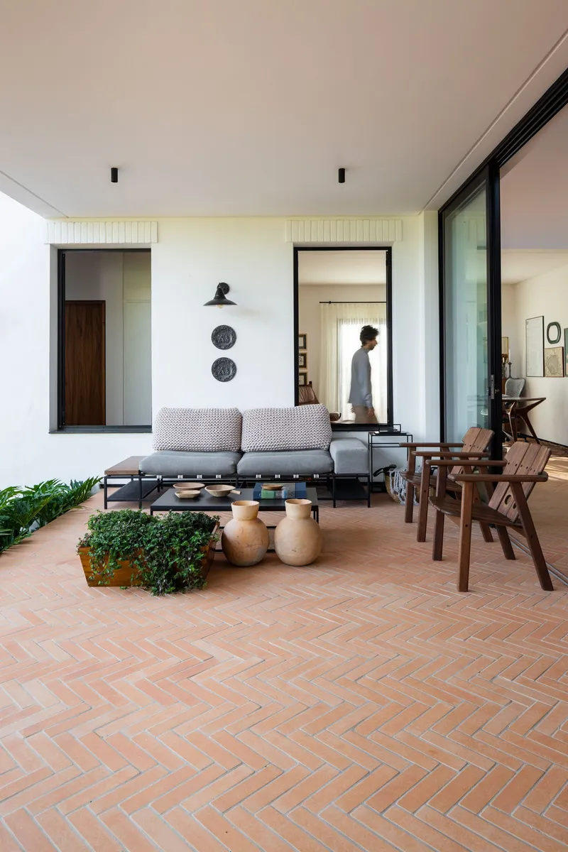 Covered terrace with herringbone brick paving and a person walking through the interior doorway