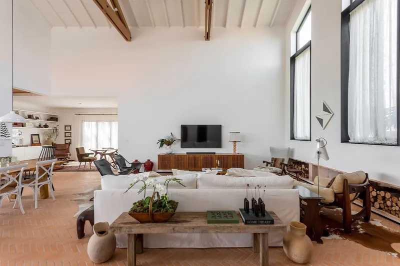 Living room with vaulted timber ceiling, white sectional sofa and firewood storage beside tall windows