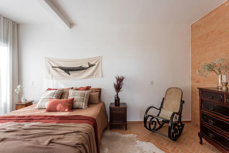Bedroom interior with exposed brick accent wall, bentwood rocking chair, and terracotta tile flooring