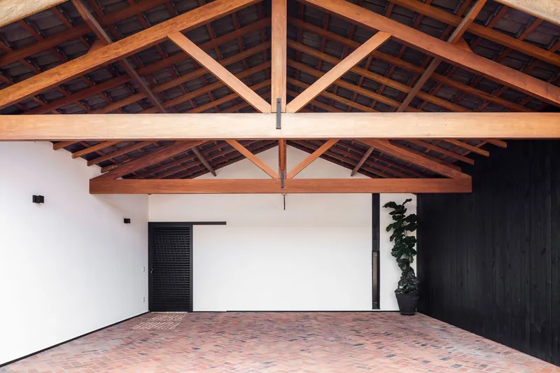 Interior space with exposed timber roof trusses, terracotta brick pavers, and dark wood cladding