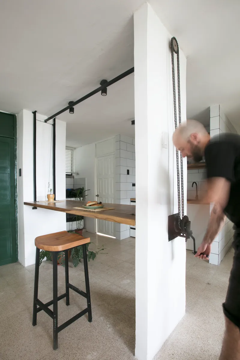 Kitchen passthrough with fold-down timber counter and a person in motion adjusting the chain mechanism