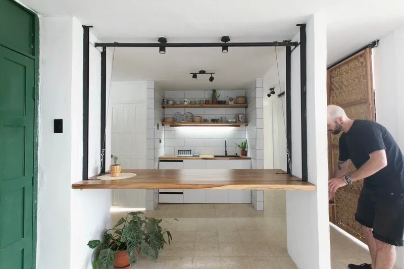 Kitchen opening framed by black steel portal and timber counter with a person standing at the doorway
