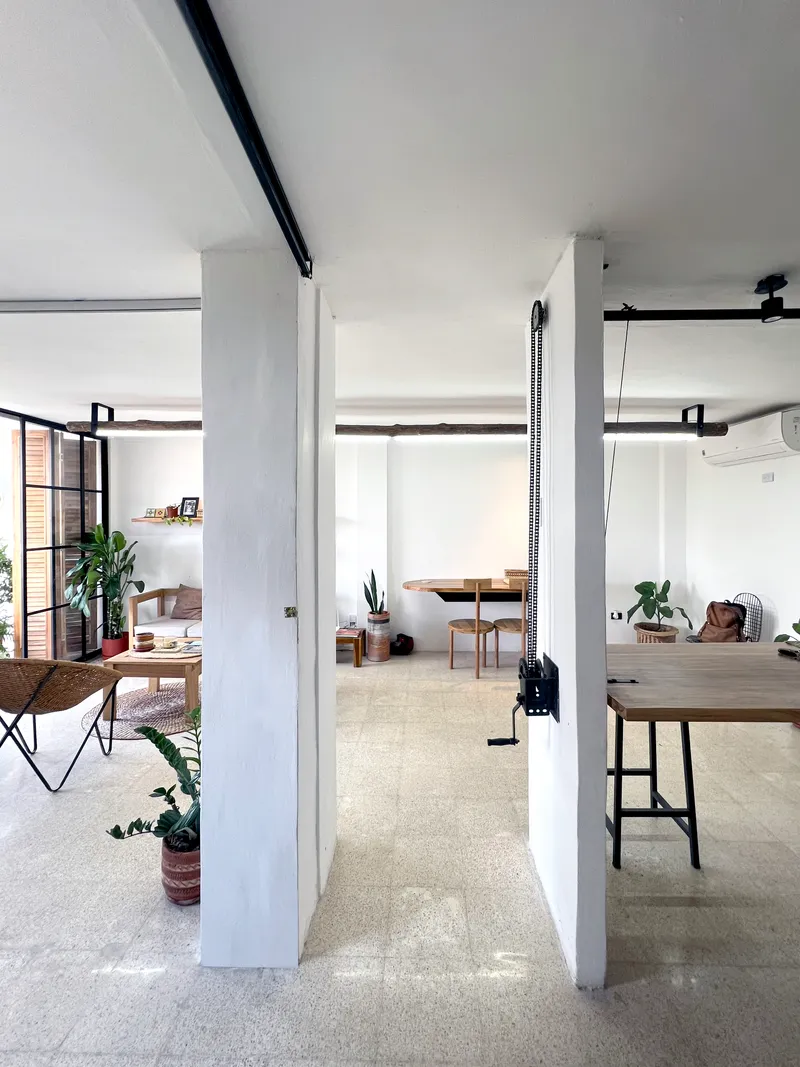 Open loft space with white columns, exposed black beams, steel-framed glazing, and terrazzo flooring