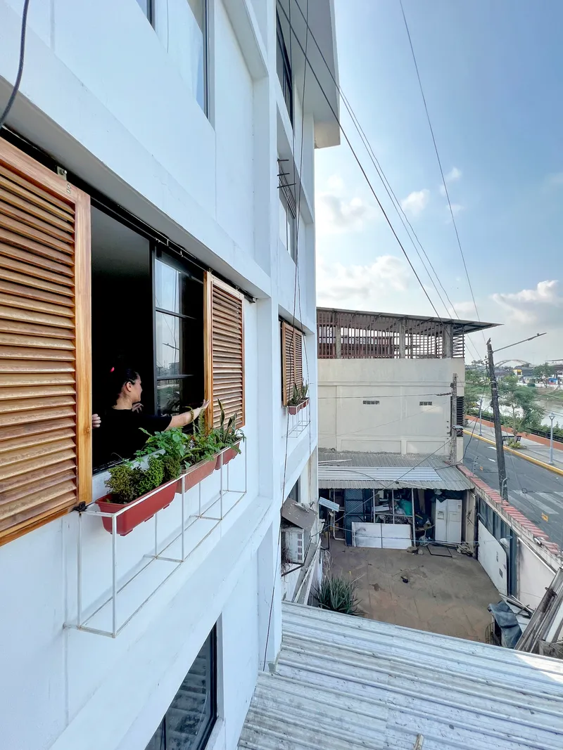 White facade with timber louvered shutters and a resident tending plants in a window box planter