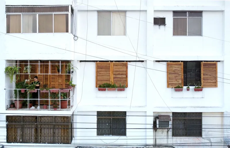 Front elevation showing timber shutters, metal security grilles, and a resident visible at a balcony