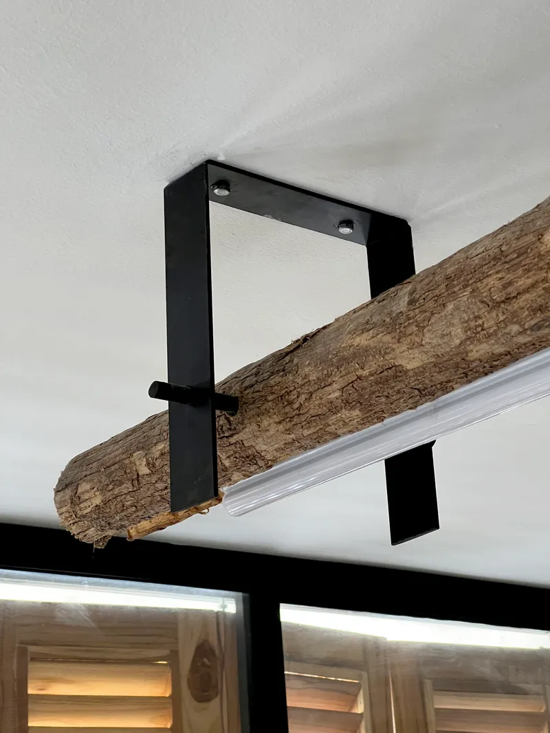 Reclaimed timber beam suspended from the white ceiling by black steel brackets with visible bolts