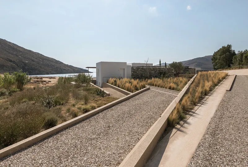 Stepped concrete pathway with gravel fill and ornamental grasses leading toward white volumes and distant hills