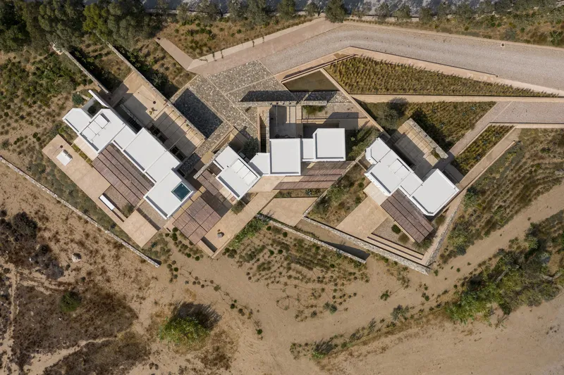 Drone view of clustered white roof volumes within stone retaining walls surrounded by cultivated fields