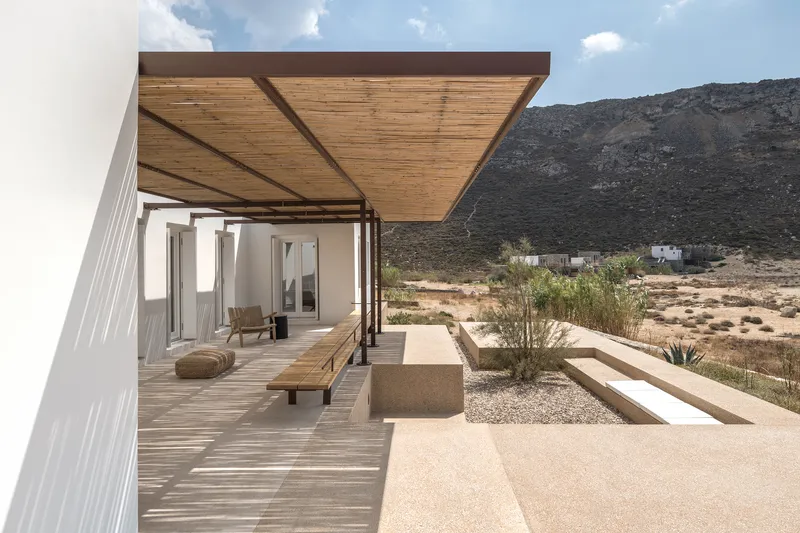 Cantilevered timber canopy over planted terrace beds with white masonry volume against arid landscape