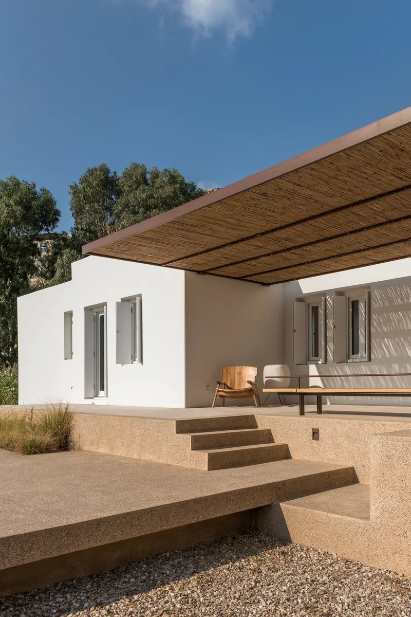 Stepped terrace platform leading to white stucco facade beneath projecting reed and steel canopy