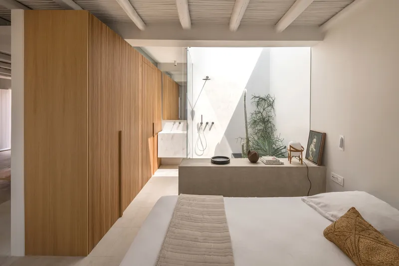 Bedroom interior with vertical timber slat partition and open courtyard bathroom beyond exposed beam ceiling
