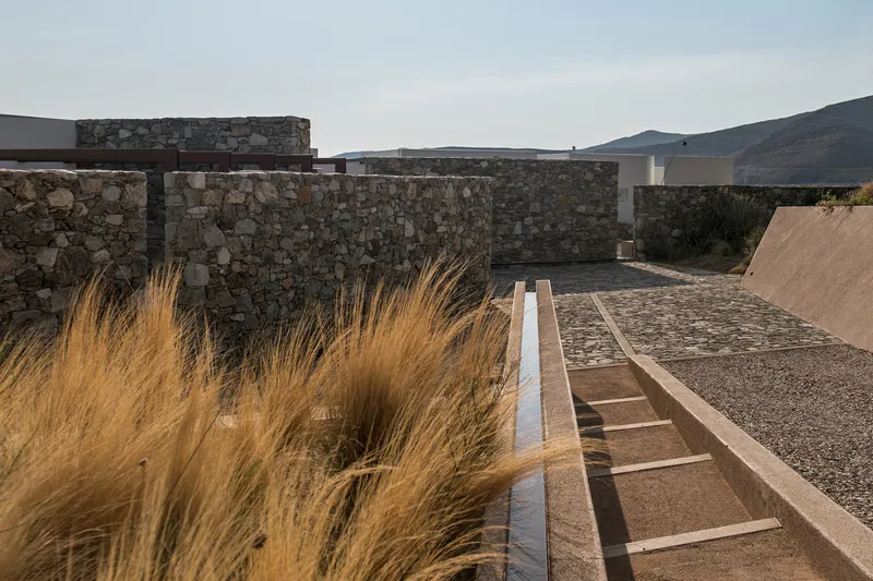 Linear water channel beside dry grasses leading toward stone walls and distant hills