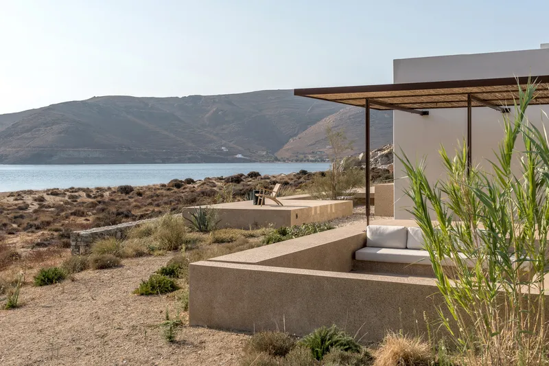 Terraced concrete seating platforms with canopy shelter framing coastal scrubland and calm bay