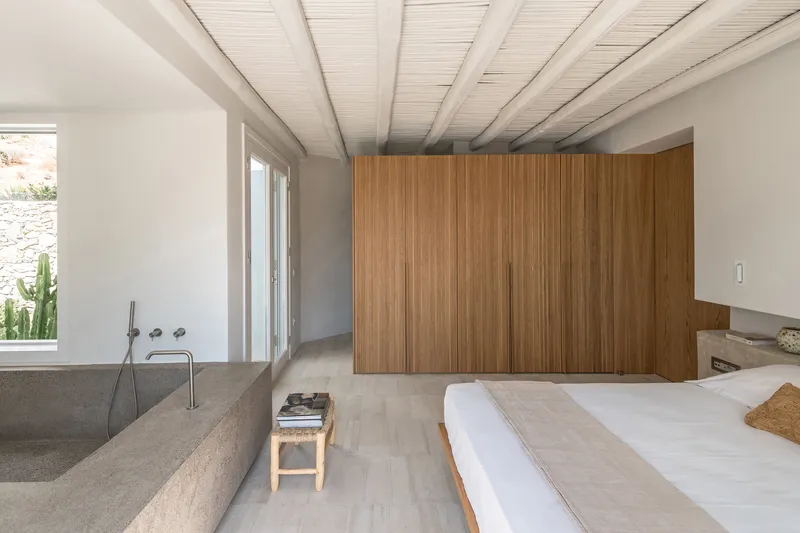 Bedroom with integrated terrazzo bathtub, vertical timber slat wall, and exposed beam ceiling in daylight