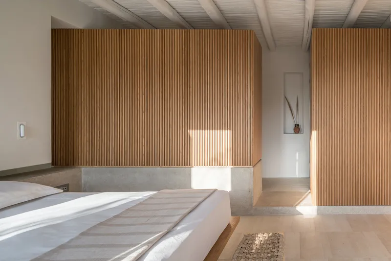 Curved timber slat wall wrapping bedroom volume with terrazzo divider in afternoon sunlight