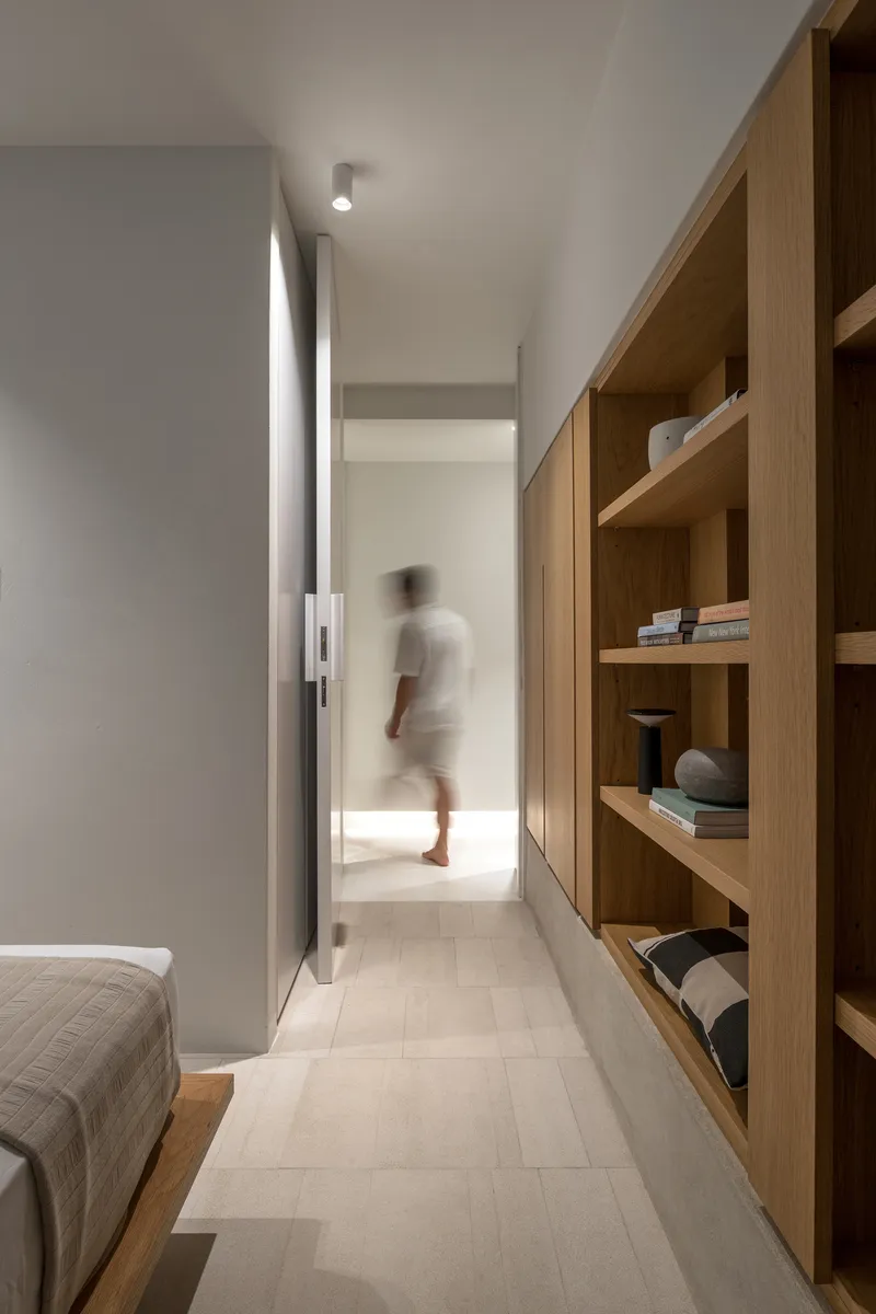 Narrow hallway with oak shelving along one wall and a blurred figure moving through distant doorway