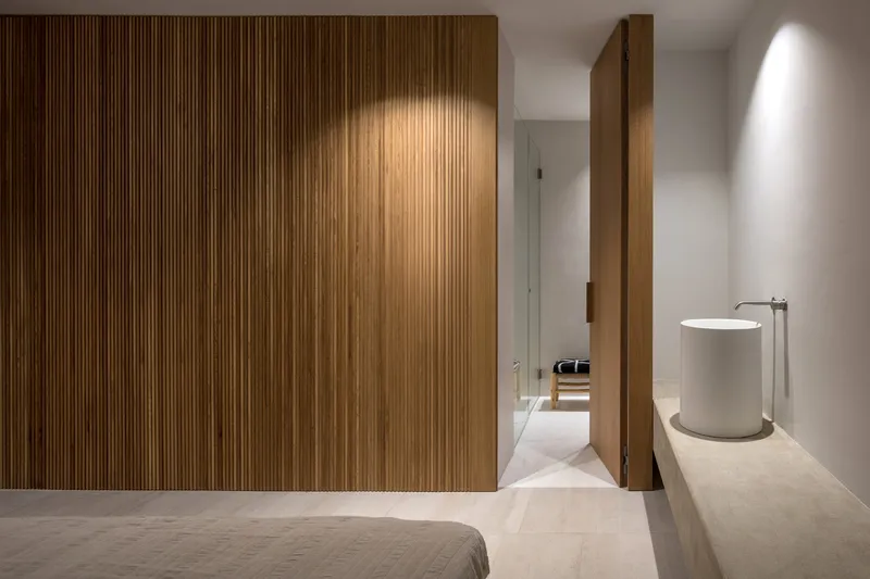 Bedroom with vertical timber slat wardrobe and white cylindrical side table under recessed lighting