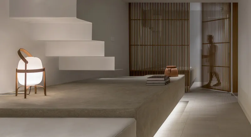 Cantilevered white plaster stairs with curved timber chair beneath and slatted wooden screens behind raised platform