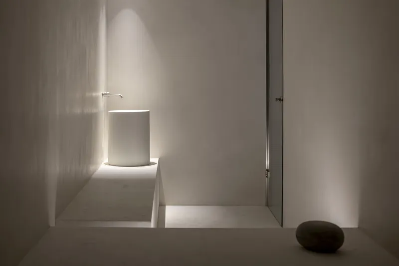 Minimalist corridor with backlit cylindrical volume and narrow slot of light along white plaster walls