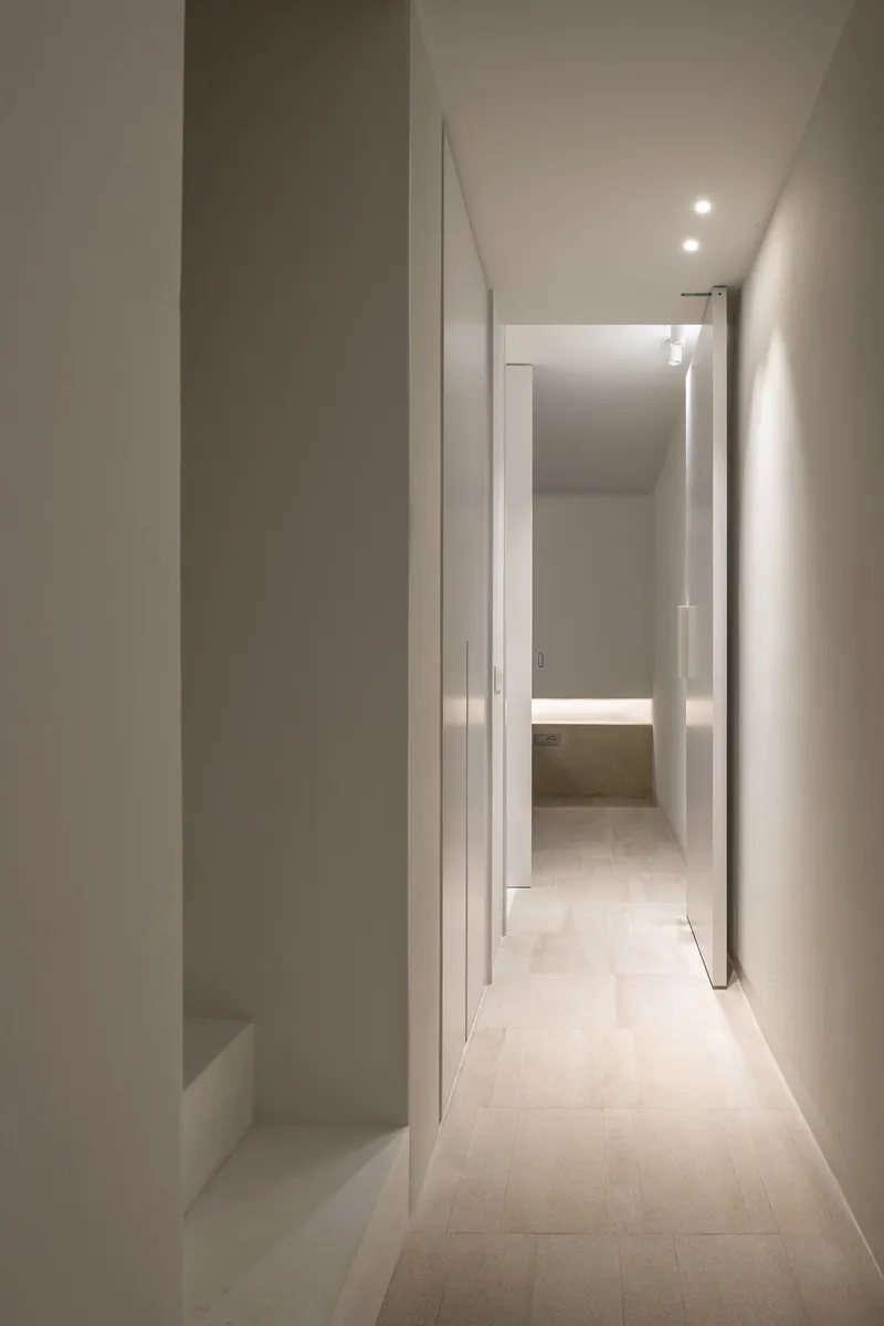 Long corridor view through layered white doorways with concealed lighting strips at floor level