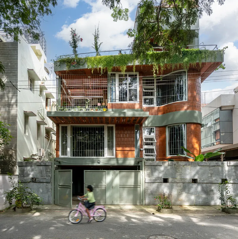 Street facade with terracotta tile cladding, rooftop garden, and child on bicycle passing by