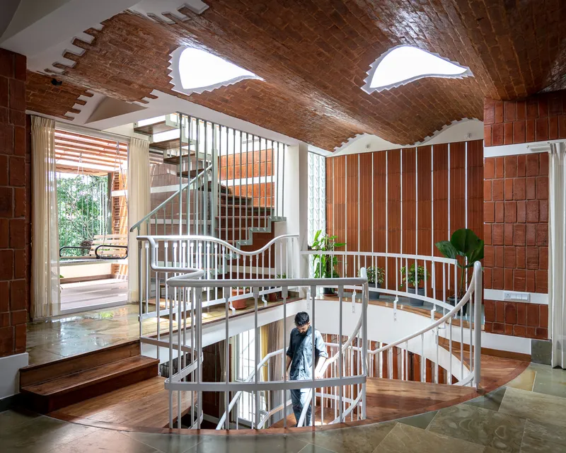 Central spiral staircase with white railings beneath vaulted terracotta tile ceiling and triangular skylights