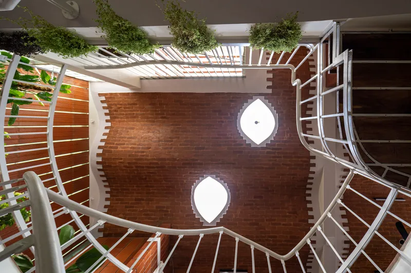 Looking down at spiral staircase with terracotta walls, diamond-shaped skylights, and hanging plants