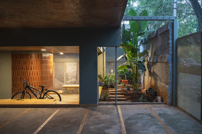 Ground-level courtyard with bicycle storage niche, perforated metal gate and banana plants at dusk