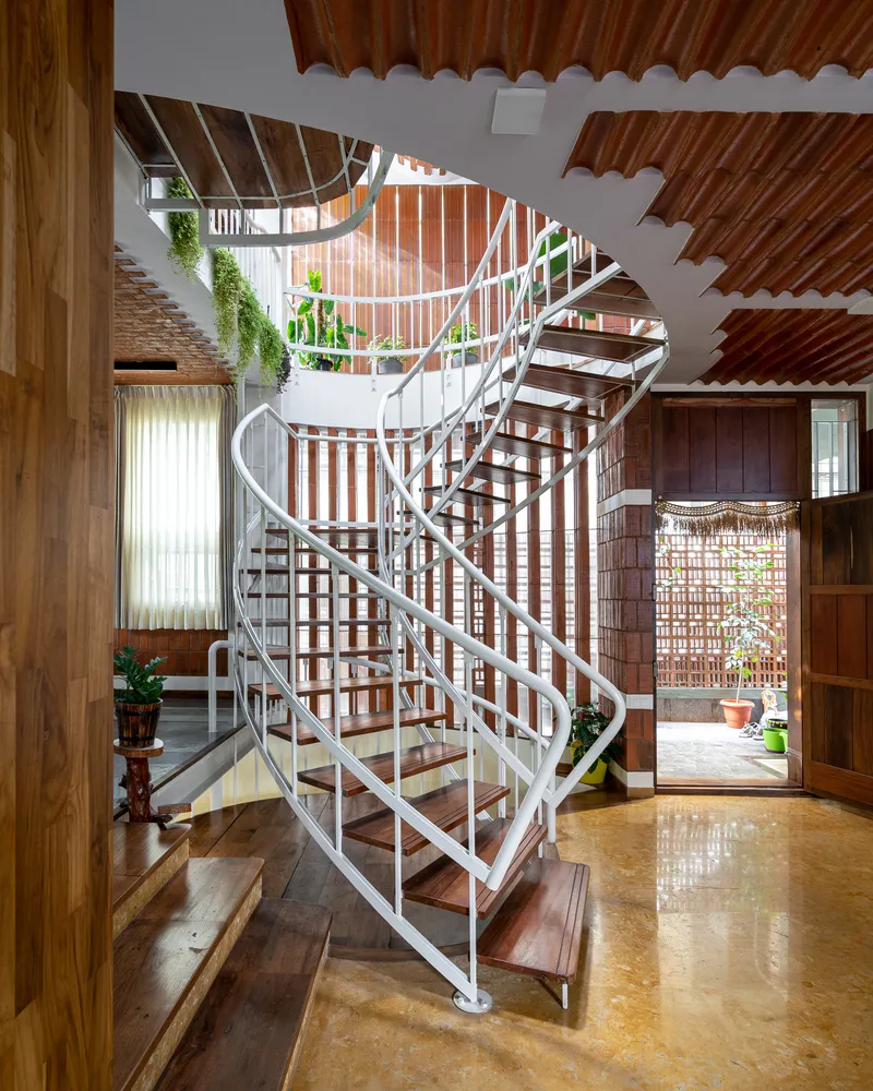 Spiral staircase rising through double-height space with terracotta tile walls and vaulted ceiling