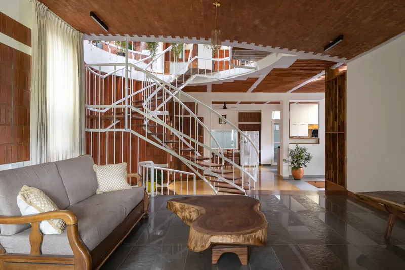 Living room view with spiral stair rising through exposed timber beam ceiling and brick tile walls