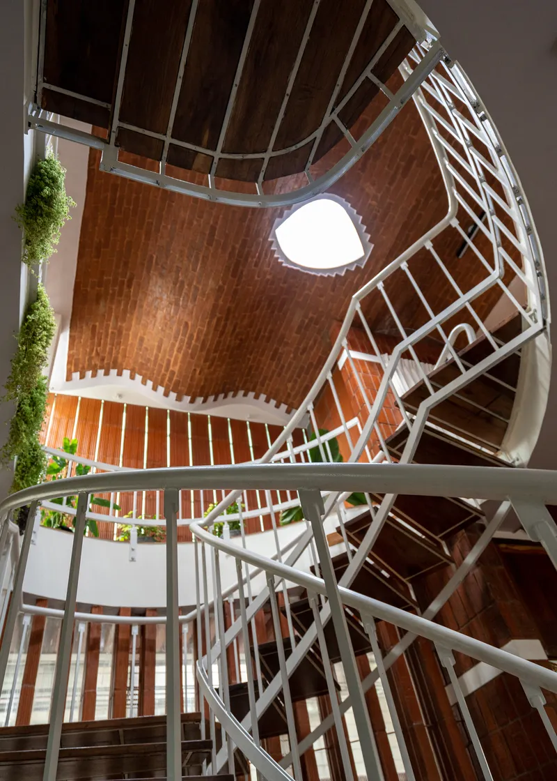 Upward view of the stair void showing white steel railings against curved brick tile walls and skylight